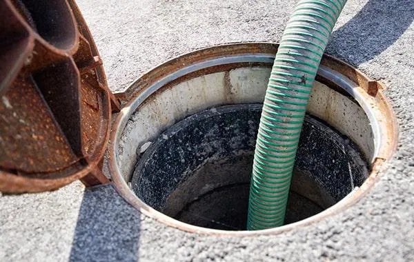 Manhole grease interceptor being serviced with a green suction hose behind a Los Angeles restaurant